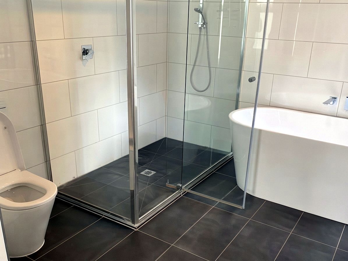 Tiled shower with glass screen, freestanding bath and neat grout lines by JT Handyman Solutionz